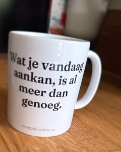 Witte keramische mok op een houten tafel met de tekst Wat je vandaag aankan, is al meer dan genoeg